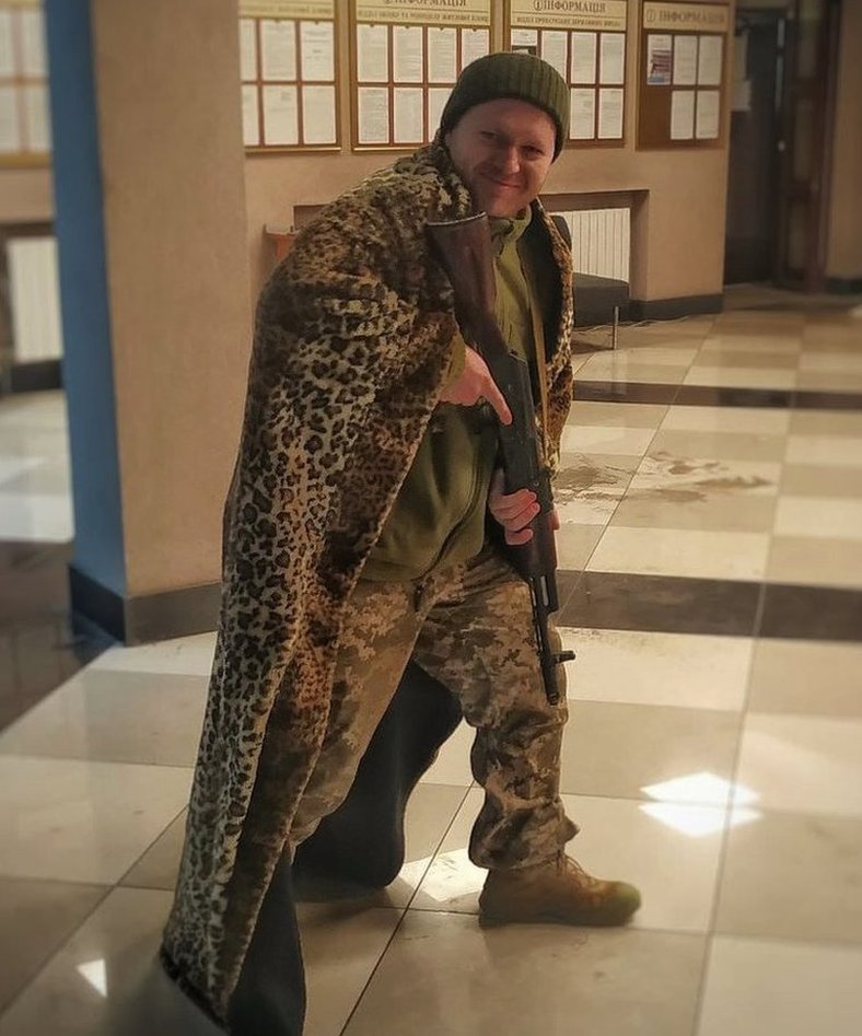 Dmitry Mrachnik holding a rifle while wearing a leopard skin blanket over his shoulders