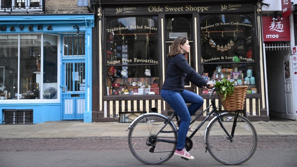 Женщина на велосипеде проезжает мимо маленьких магазинчиков в Кембридже