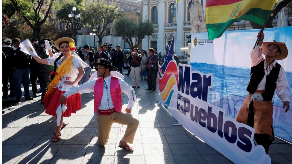 Bolivianos bailan frente a un cartel en el que se lee: "Mar para los pueblos".