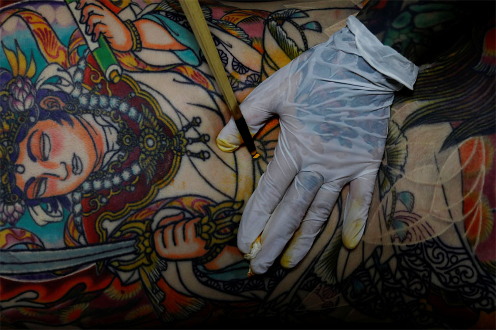 A tattoo artist works on a customer`s back