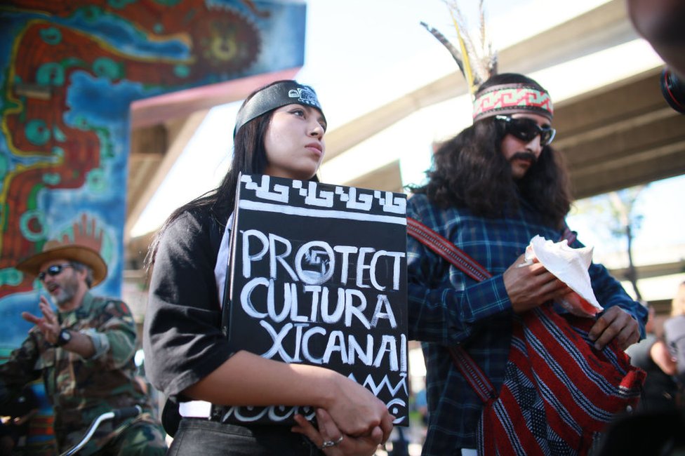 Mujer sostiene un cartel que llama a la protección de la cultura chicana en Chicano Park, San Diego.