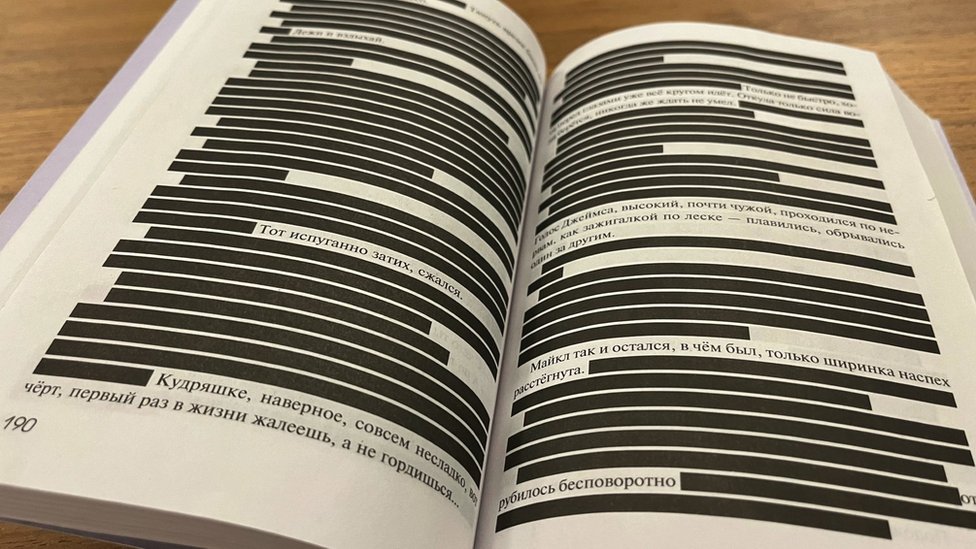 Um livro aberto com tarjas pretas cobrindo a maioria das linhas de texto