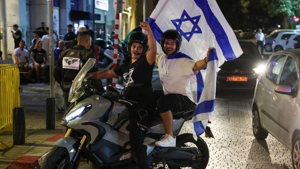 People cheer and wave an Israeli national flags as they celebrate the news of the death of Hamas leader Yahya Sinwar, in the Israeli costal city of Netanya, on October 17, 2024.