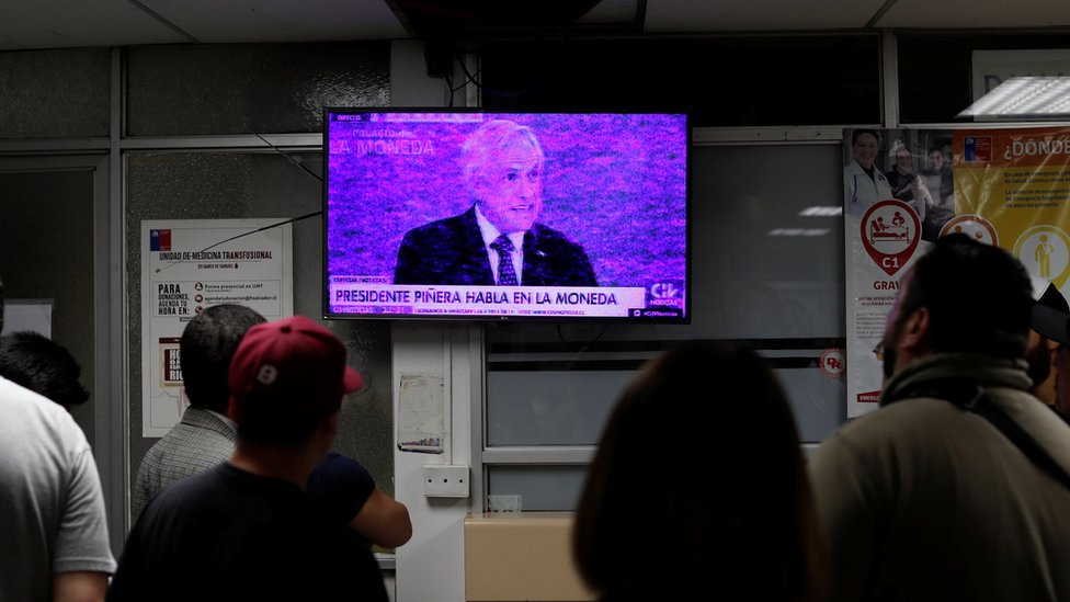 Люди смотрят телевизор, транслирующий выступление президента Чили Себастьяна Пинеры в отделении неотложной помощи больницы на фоне антиправительственных протестов в Сантьяго, Чили, 12 ноября 2019 г.