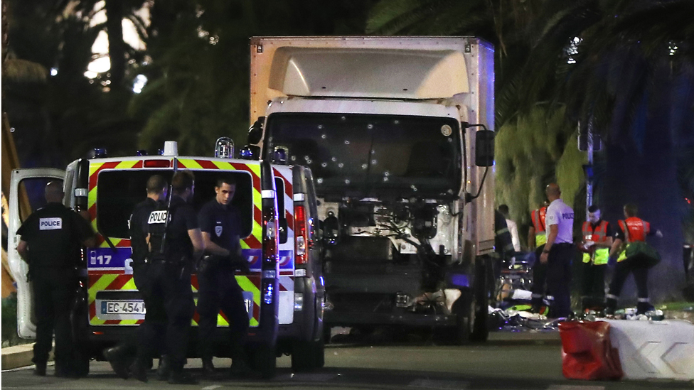 Полицейские и спасатели стоят возле фургона, который врезался в толпу, оставившую фейерверк в городе Ницца на Французской Ривьере 14 июля 2016 года.