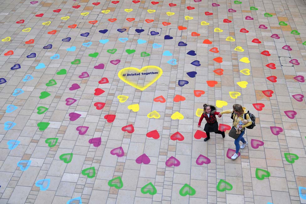 A mother and daughter walk over a spiral pattern of rainbow-coloured hearts