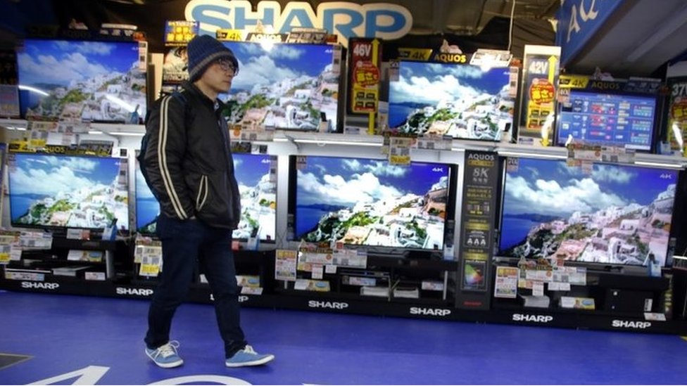 Покупатель идет перед плоскопанельными телевизорами Sharp Aquos в магазине электроники в Токио в четверг, 25 февраля 2016 г.