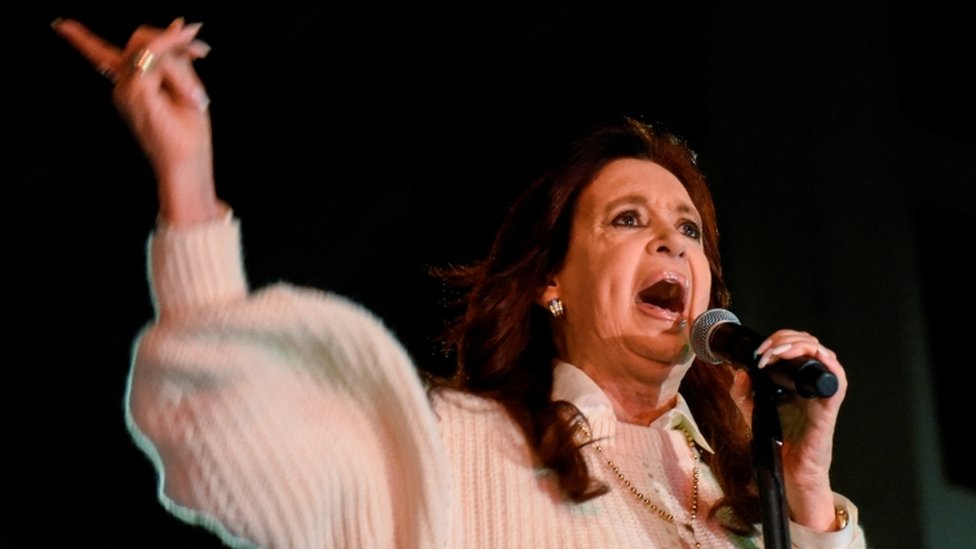 Kirchner gesticula enquanto fala no microfone, em evento à noite