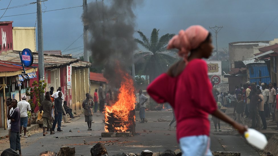 Женщина проходит мимо горящей баррикады во время демонстрации против в Бужумбуре, Бурунди, май 2015 г.