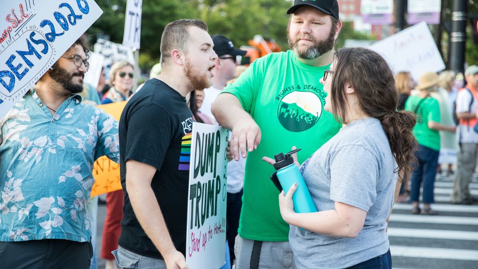 美國新罕布什爾州曼徹斯特一場聲援特朗普集會會場外綠衣男子嘗試調停在吵架的支持特朗普黑衣男子（左）與反特朗普灰衣女子（女）（15/8/2019）