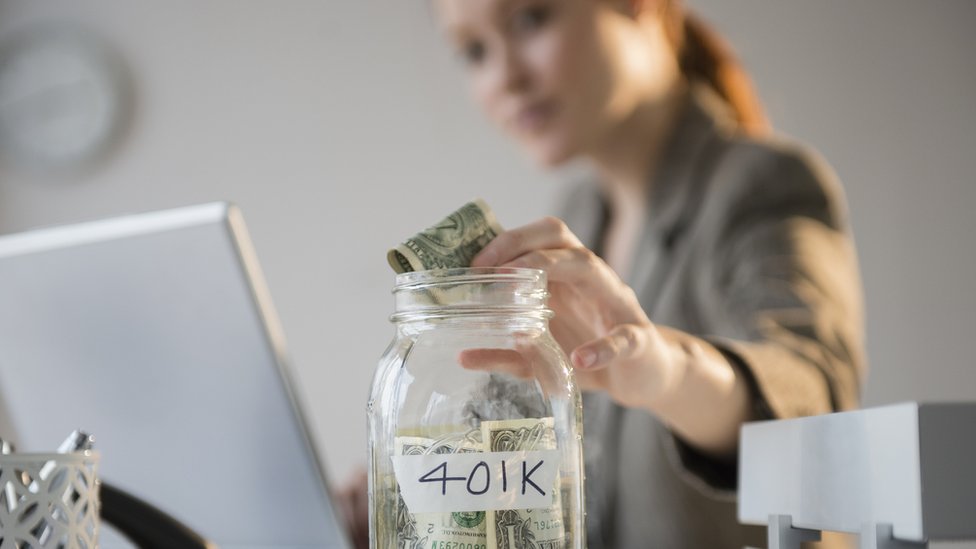 Una mujer colocando dinero en un bote con una etiqueta que dice 401K.