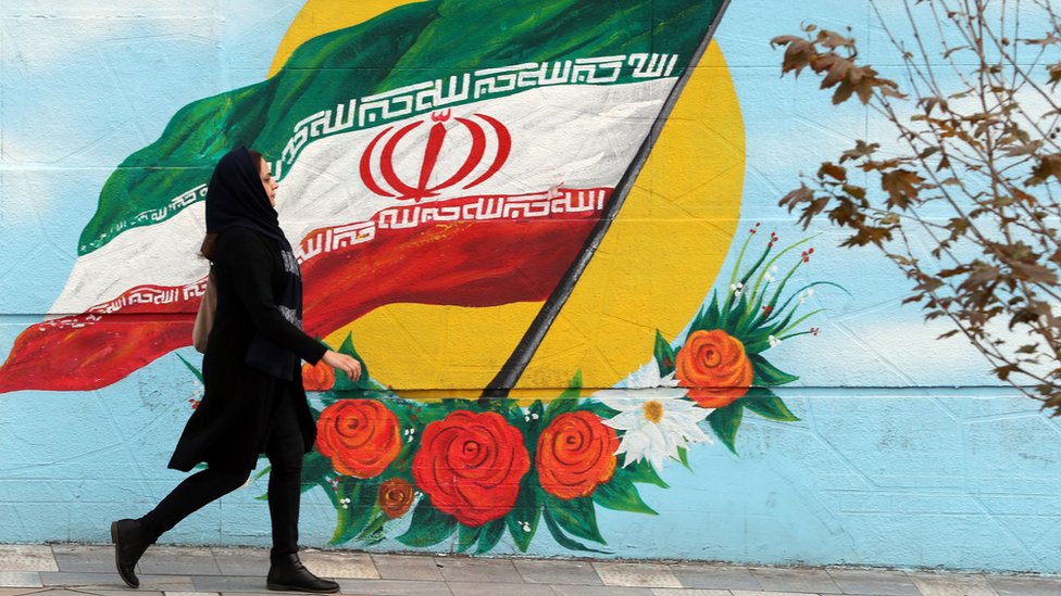 Женщина идет перед фреской с изображением флага Ирана