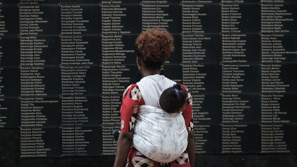 Женщина с ребенком на руках смотрит на стену с именами жертв, когда Руанда отмечает 25-ю годовщину геноцида 1994 года у Мемориала геноцида Кигали в Кигали, Руанда - 8 апреля 2019 года