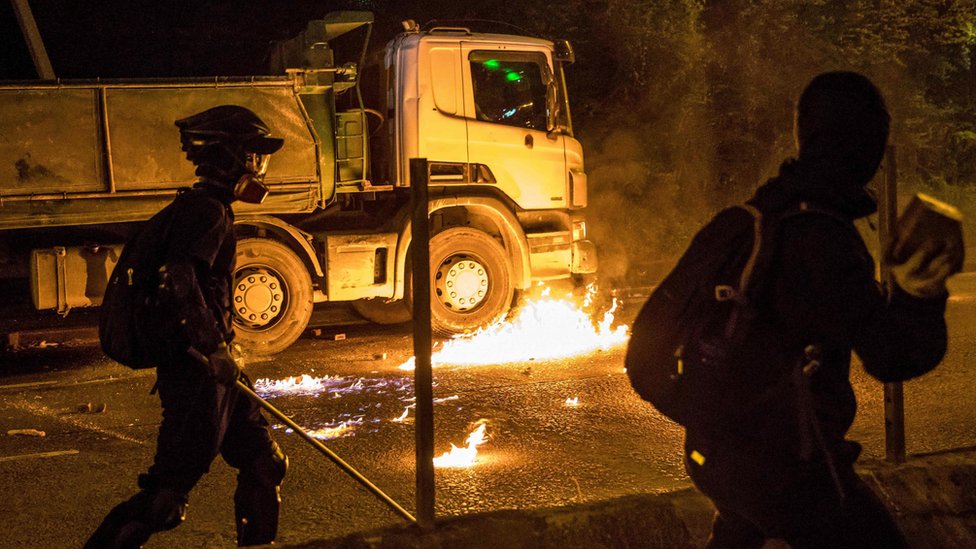 Бомба с бензином, брошенная протестующим, горит рядом с грузовиком после того, как водитель попытался проехать по заблокированной дороге за пределами Гонконгского политехнического университета 14 ноября 2019 года.