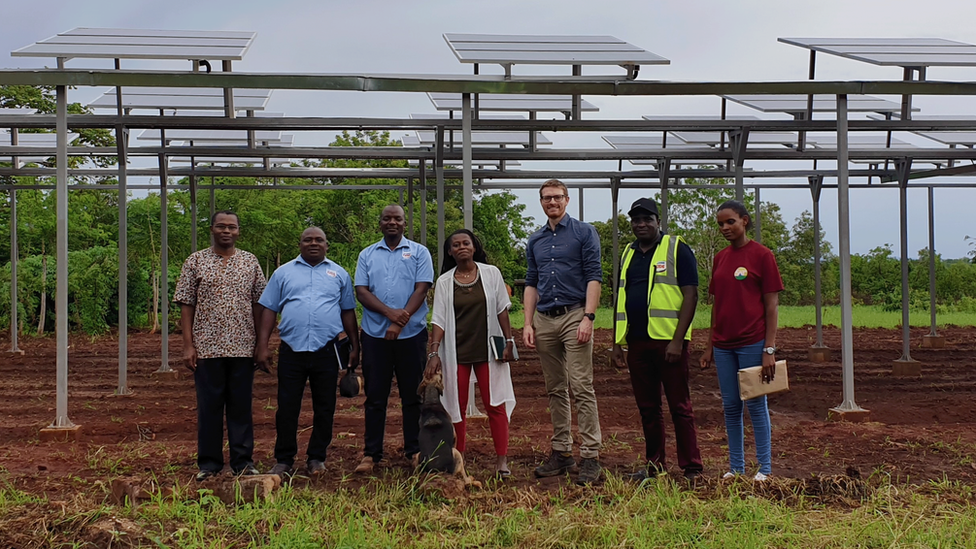 Elevated solar panels several metres high in an agricultural field in Tanzania with a group of people from the project posing in front