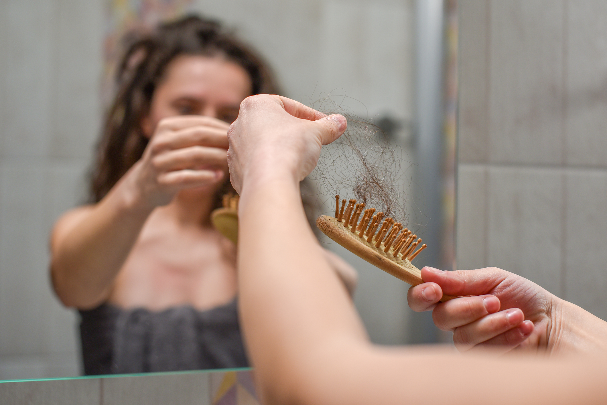 Mulher em frente ao espelho com escova cheia de cabelo