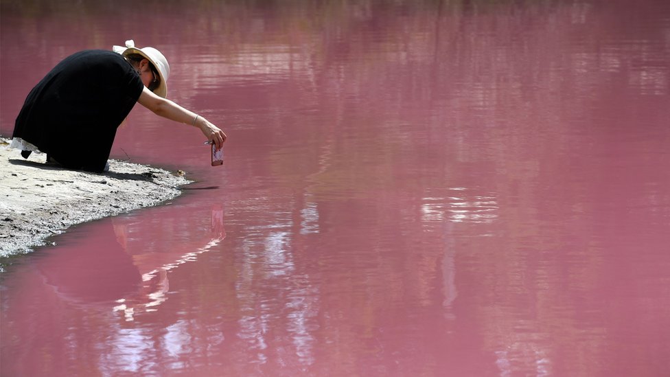 Žena kleči ispred samo jezera i fotografiše telefonom