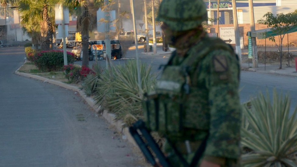 Agente militar en Culiacán, Sinaloa, tras la detención de Ovidio Guzmán, mira un vehículo incendiado al final de la calle.