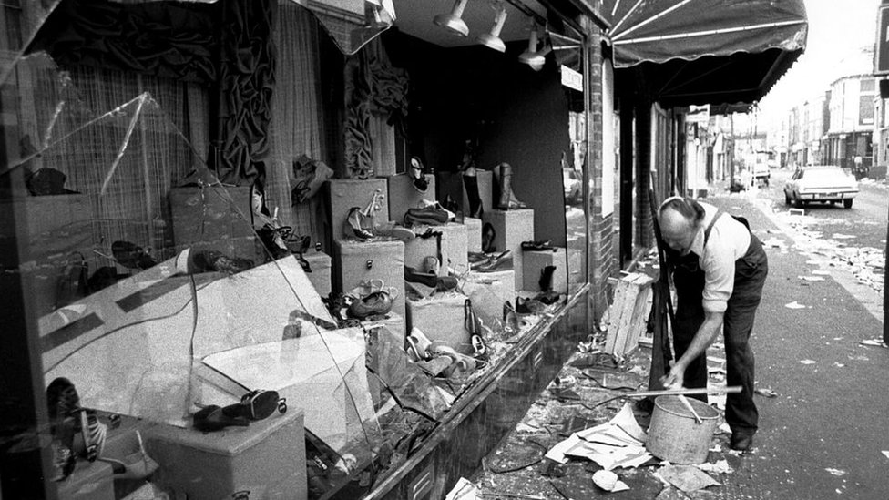 Un comerciante de Londres recoge los vidrios de la vitrina de su tienda que fue destruida durante un disturbio