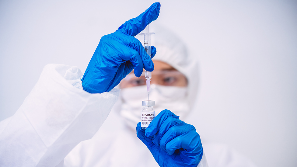 Scientist with syringe and bottle marked "Covid 19"