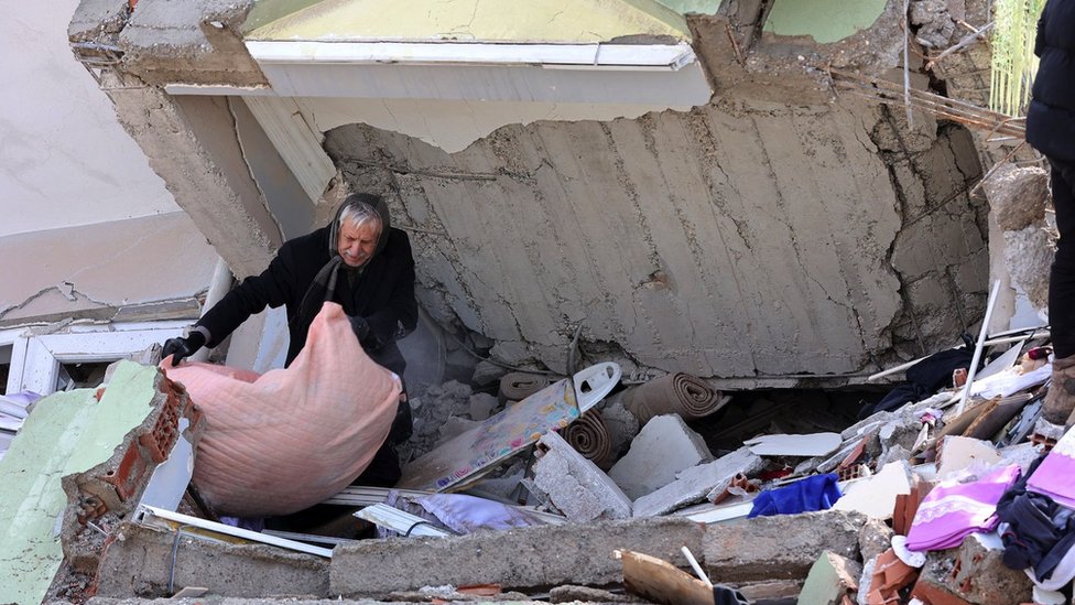 A man gathers a blanket under a collapsed building in Kahramanmaras, Turkey