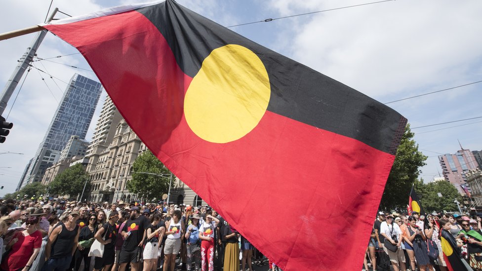 Протестующие несут флаг аборигенов над маршем в Мельбурне в День Австралии в 2019 году