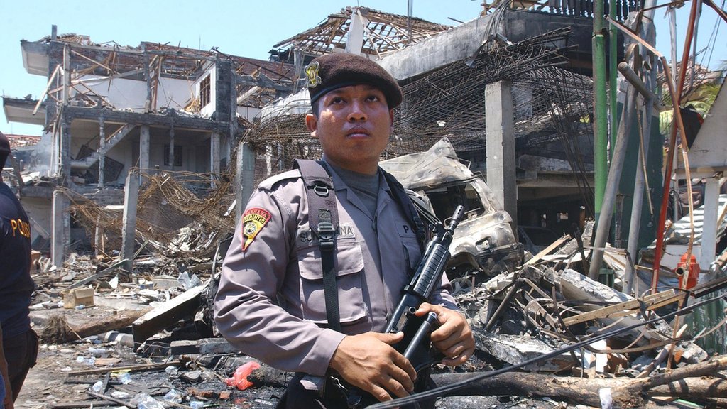 Вооруженный индонезийский полицейский охраняет остатки ночного клуба после взрыва на Бали в октябре 2002 года.