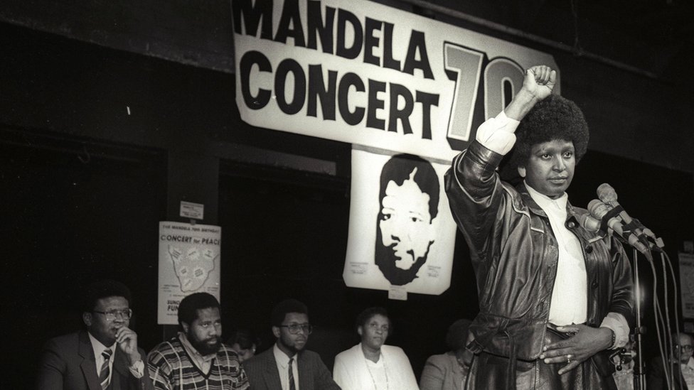 Винни Мандела поднимает кулак в знак приветствия черной власти после того, как объявила, что в 1988 году состоится массовый поп-концерт в честь 70-летия ее мужа