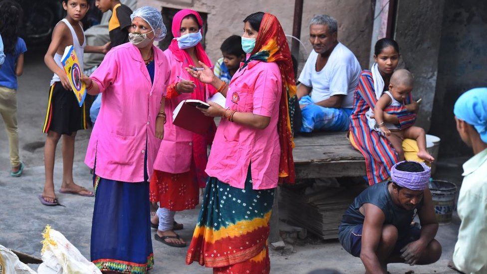 Медицинские работники Asha разговаривают между собой, проводя опрос от двери до двери для выявления случаев заболевания Covid-19, поскольку колония JJ в Патпаргандже уже сообщила о более чем 70000 случаев заболевания недалеко от Маюр Вихар 25 июня 2020 года в Нью-Дели, Индия