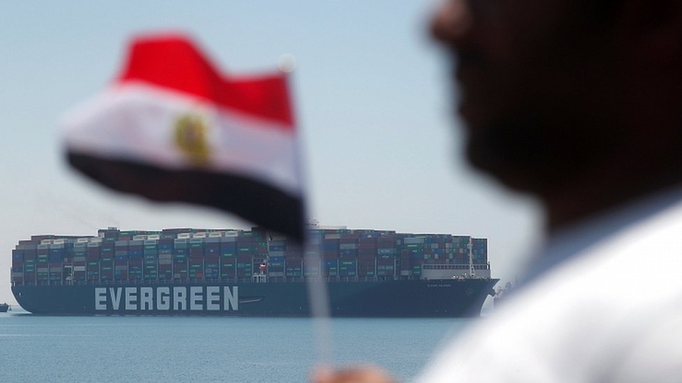 A man holds an Egyptian flag as Ever Given is seen at the Suez Canal in Egypt"s Great Bitter Lake in Ismailia, Egypt, July 7, 2021