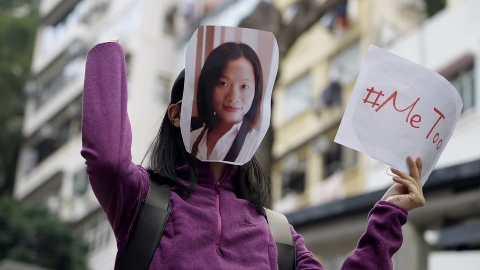 Protester holds MeToo placard and wears mask with Huang's face on it