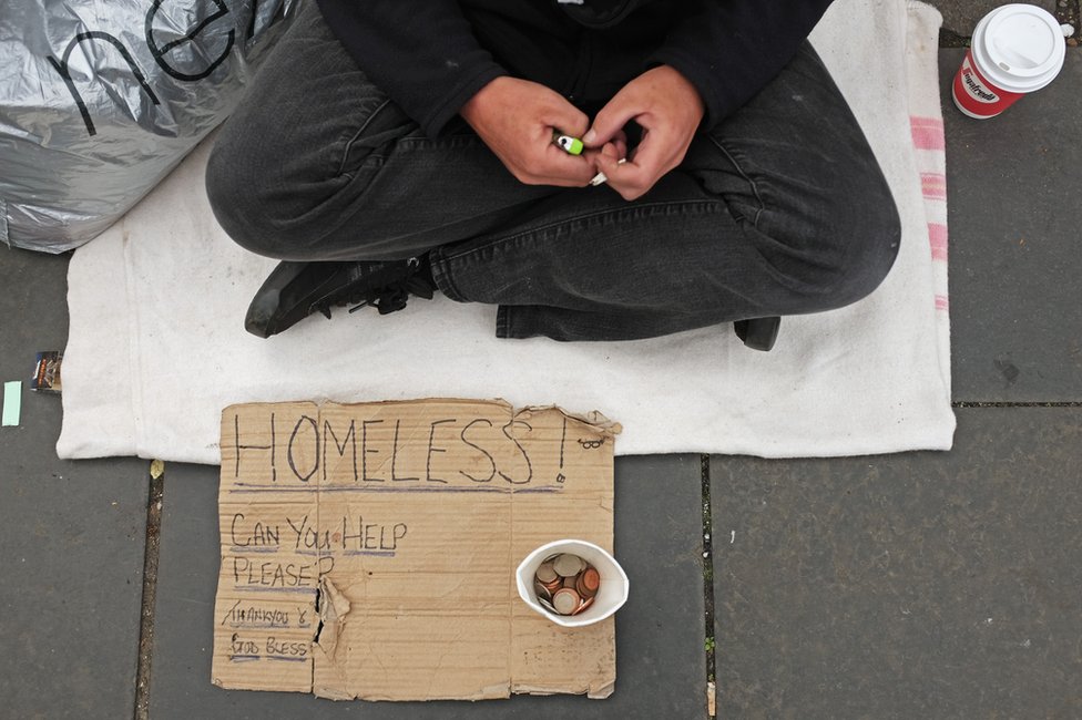 Руки, знак и денежный стаканчик бездомного