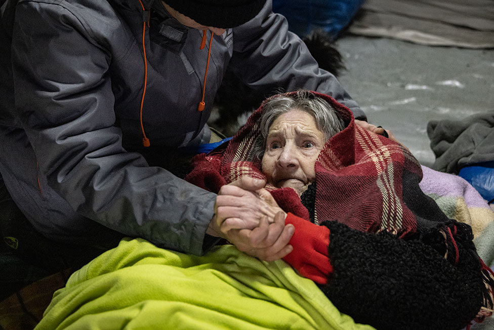 صورة في 8 مارس - امرأة مسنة تتلقى المساعدة بينما يعبر الأوكرانيون طريقًا مرتجلًا على طول جسر مدمر للفرار من مدينة إيربين يوم الثلاثاء. يوم الجمعة