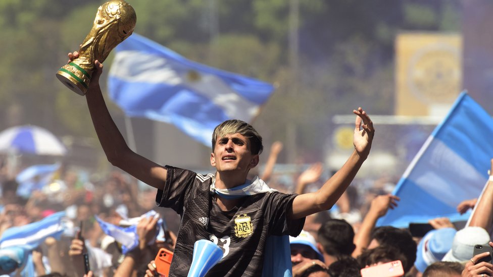 Un muchacho alza una réplica de la copa del Mundial y celebra en las calles de Buenos Aires.