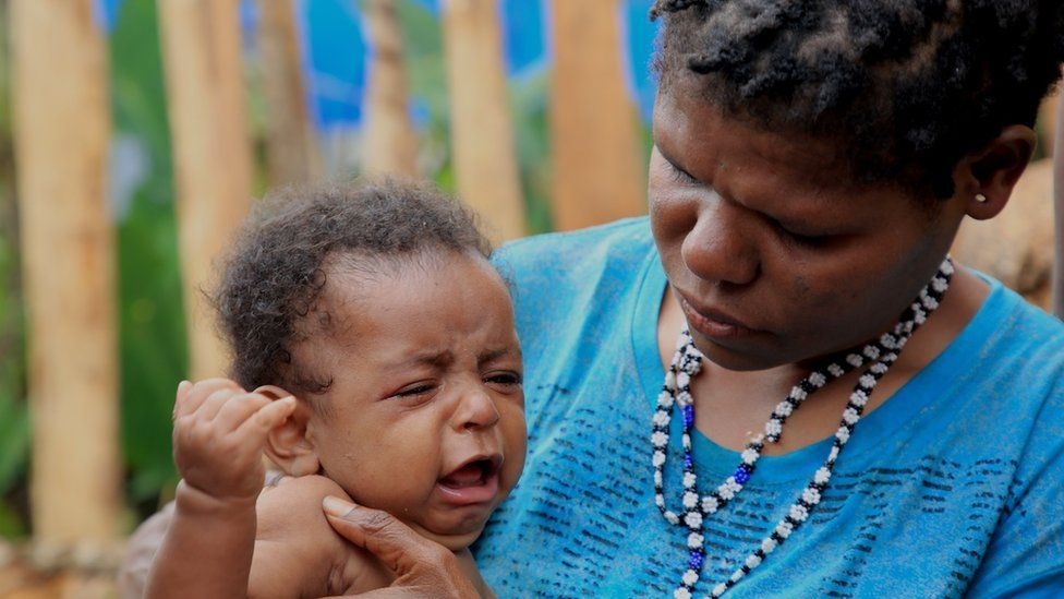 Джубиана Когея держит плачущего ребенка на руках