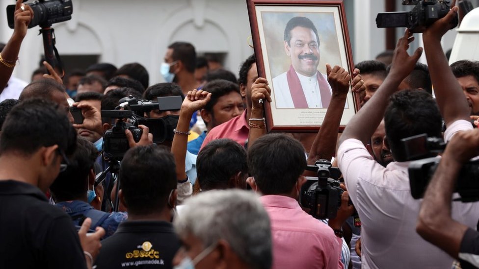 Pro-government supporters hold Prime Minister Mahinda Rajapaksa's portrait while protesting outside the prime minister's residence while people film and take photos