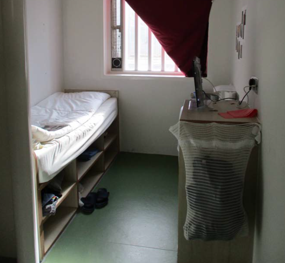 Тюремная камера с односпальной кроватью и решетками на окнах