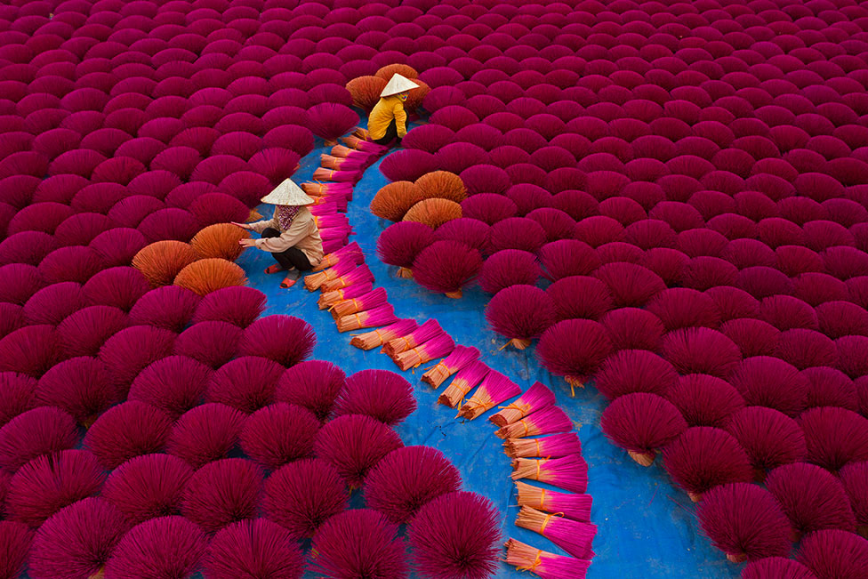 Workers sit surrounded by thousands of incense sticks