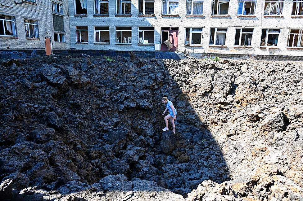 امرأة تقف في حفرة تسبب بها سقوط صاروخ في ملعب مدرسة في منطقة سكنية في مدينة خاركيف الأوكرانية.