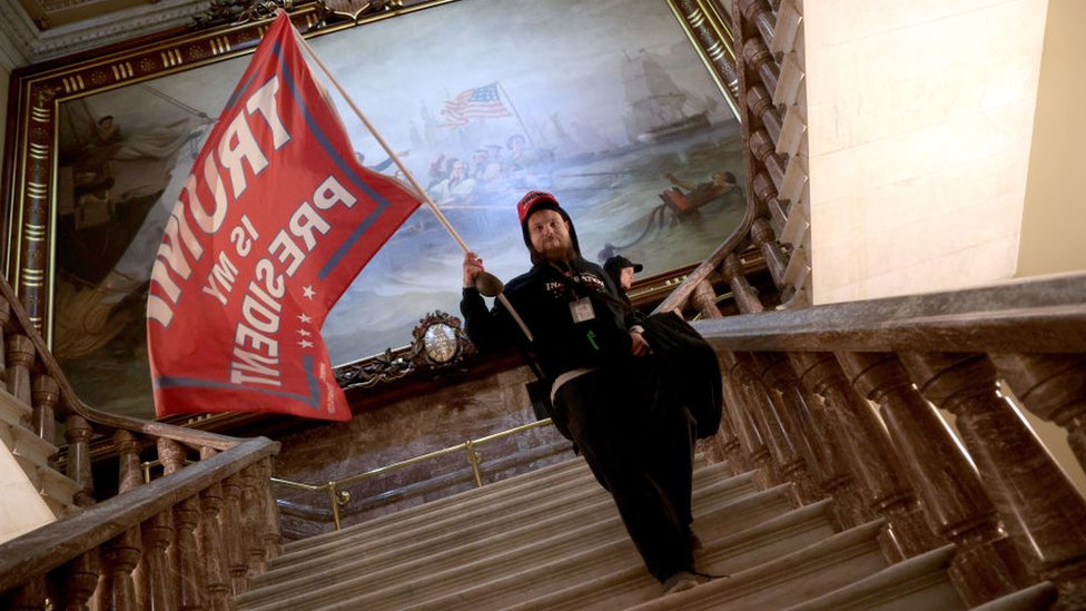 Un simpatizante de Donald Trump sostiene una bandera en apoyo al presidente mientras baja por las escaleras de una sección del Capitolio de Estados Unidos tras haber tomado el edificio.