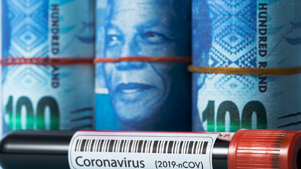Связки банкнот из южноафриканских рандов с изображением лица Нельсона Манделы, помещенные за флакон с кровью, обозначенной коронавирусом