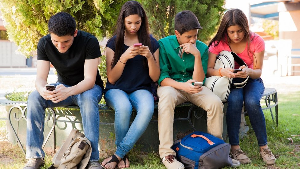 Un grupo de adolescente mirando sus pantallas en lugar de hablar entre ellos.