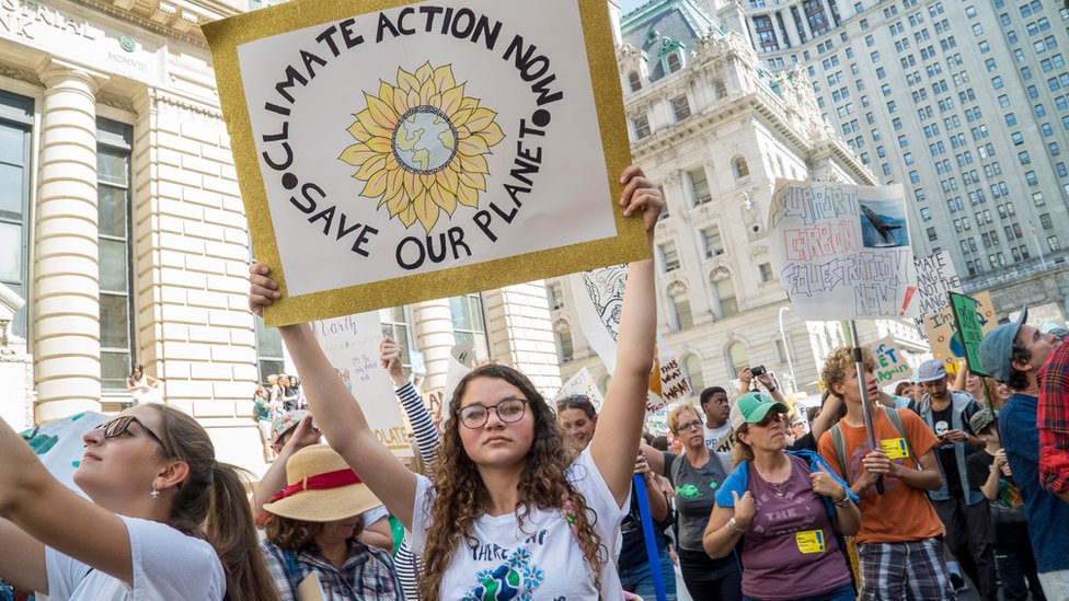 Jóvenes marchando en la calle con un cartel que pide acciones urgentes contra el cambio climático