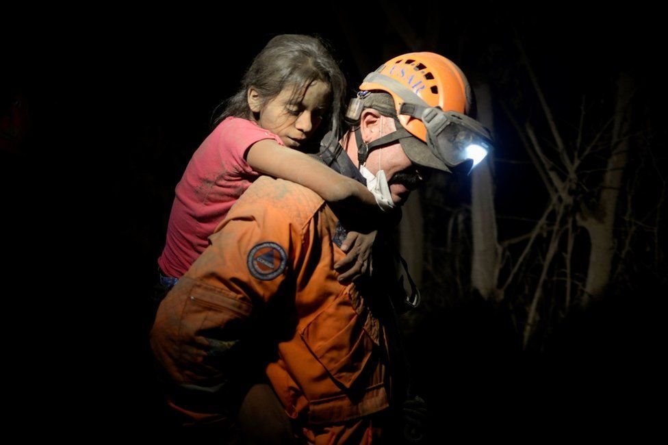 أحد عناصر قوات الانقاذ يجلي فتاة من موقع ثوران البركان