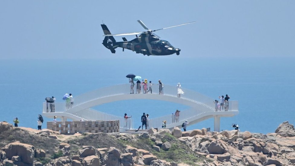 Turistas en la isla china de Pingtan, la más cercana a Taiwán, observan un helicóptero militar durante las maniobras de su país en respuesta al viaje de Pelosi