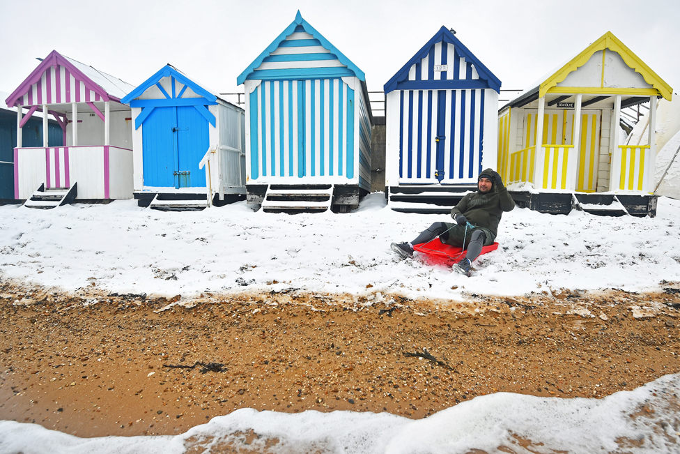 A man sits on a sledge on the snow-covered beach at Thorpe Bay, Essex, on 9 February 2021