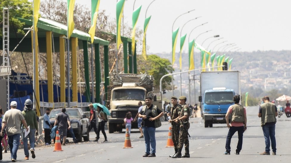 Soldados, pessoas e caminhões em avenida de Brasília, onde se vê enfeites em verde e amarelo