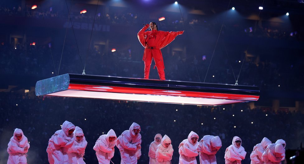 Rihanna en una plataforma flotante sobre un enjambre de enérgicos bailarines vestidos de blanco