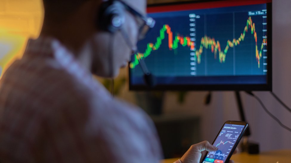 روسيا وأوكرانيا: من استفاد من العملات الرقمية في الحرب؟ 1 رجل يتابع عملات رقمية على حاسوب وهاتف