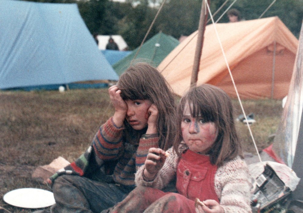Двое детей сидят на земле с палатками позади них